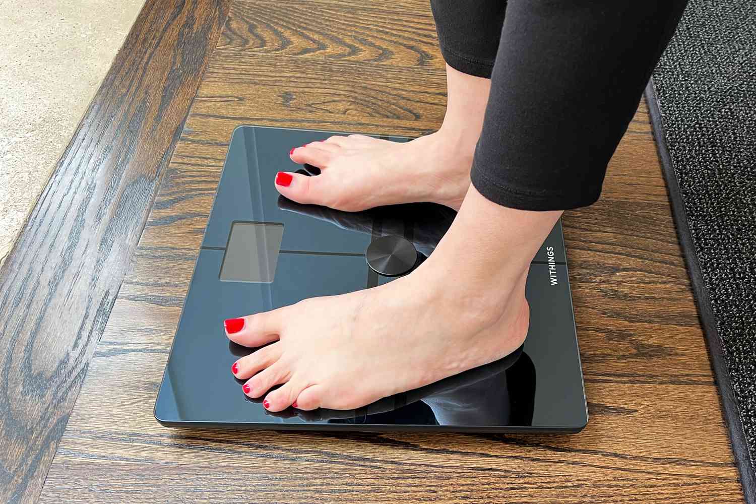 Bare feet on the Withings Body Comp Smart Scale placed on wood floor